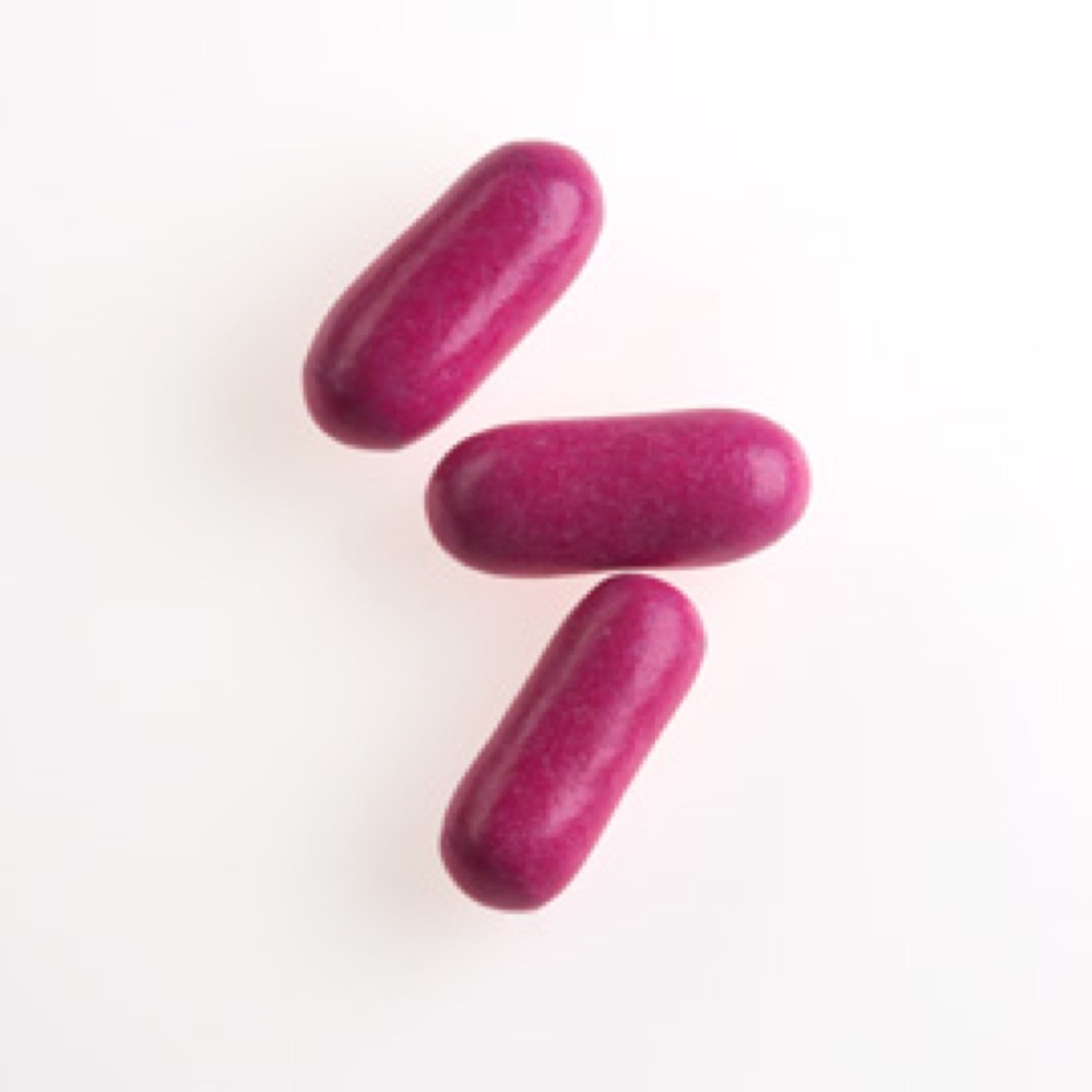 Three long, shiny, purple-colored capsules positioned on a white surface.