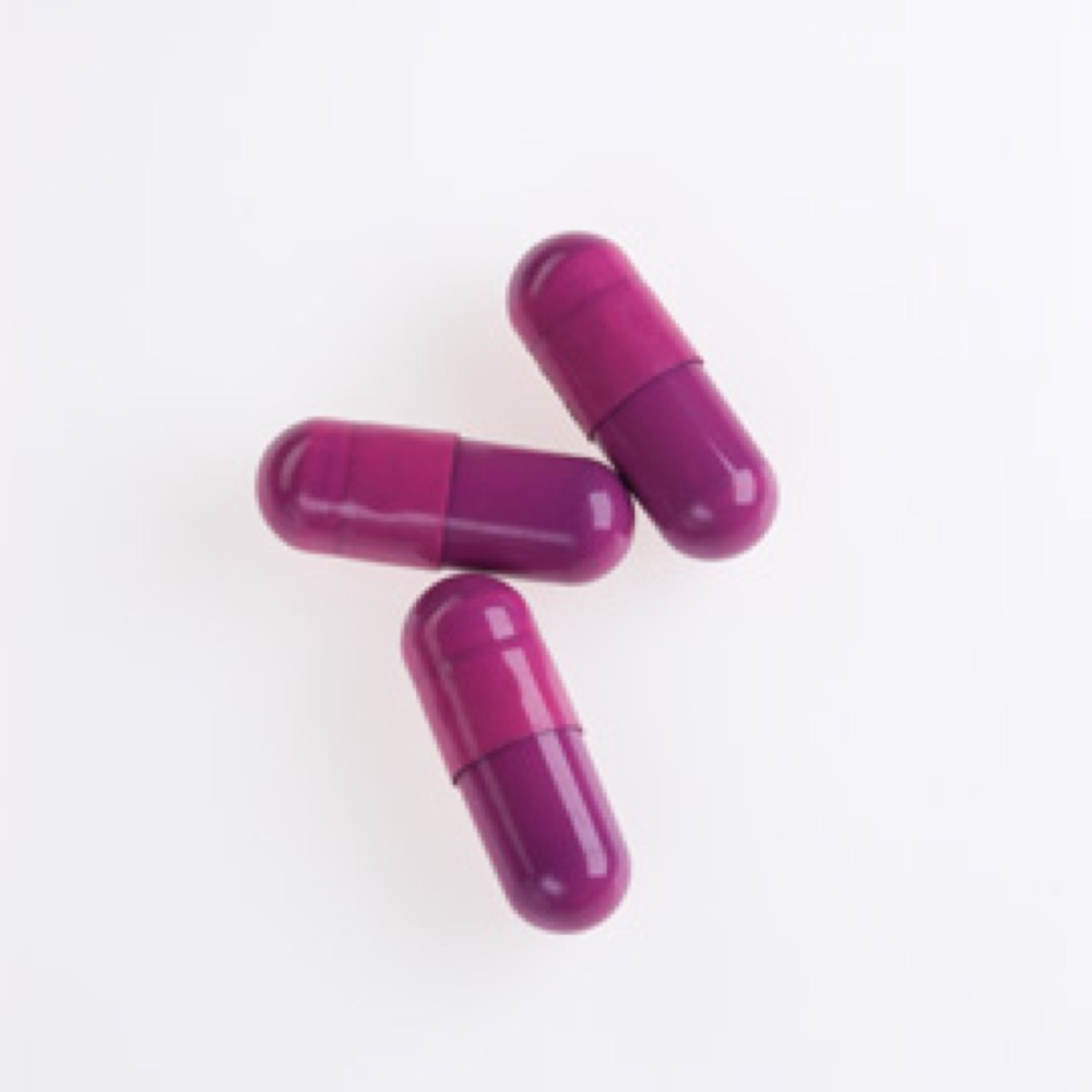 Three long, shiny, purple-colored pull apart and fill gelatin capsules positioned on a white surface.
