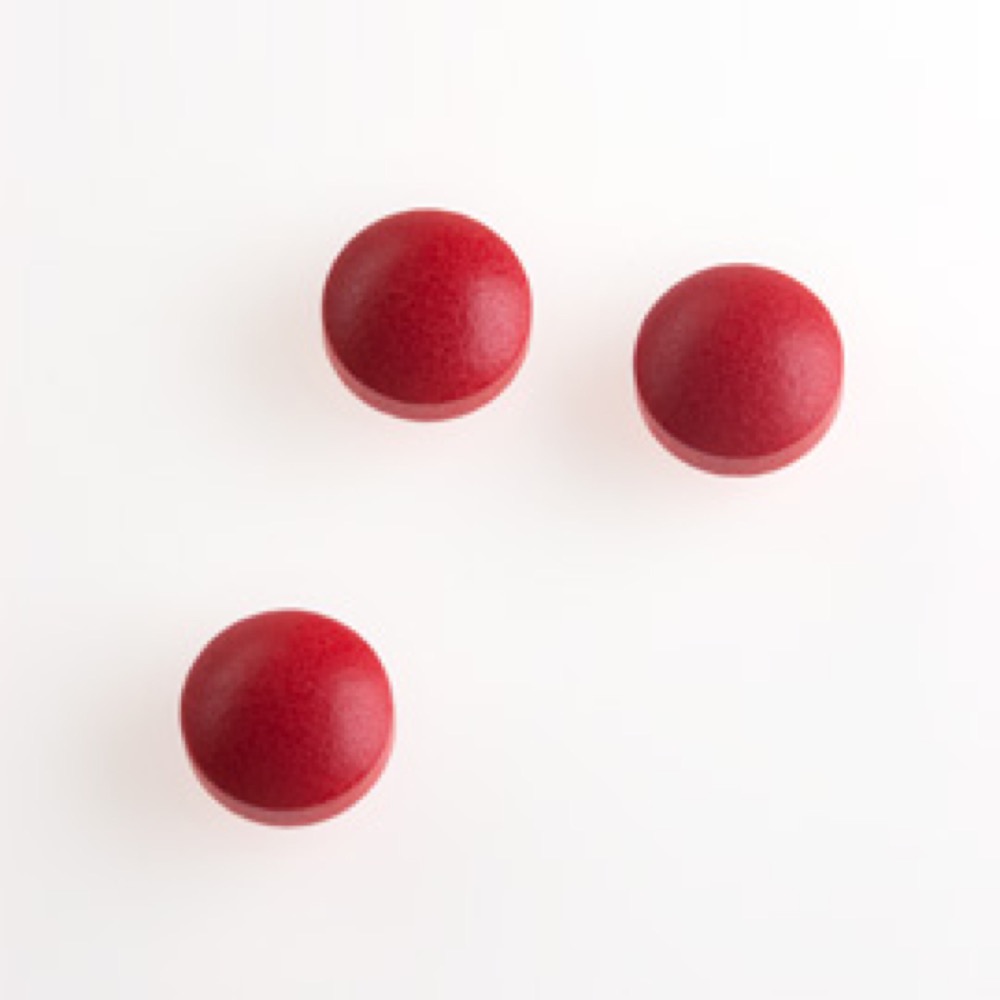 Three circular, dark red colored pills, that are matte texture against a white background.